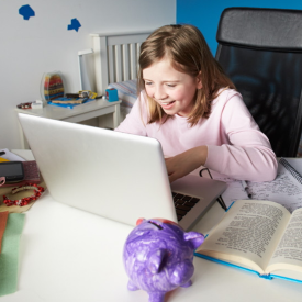 Pige sidder ved skrivebod med computer og bog